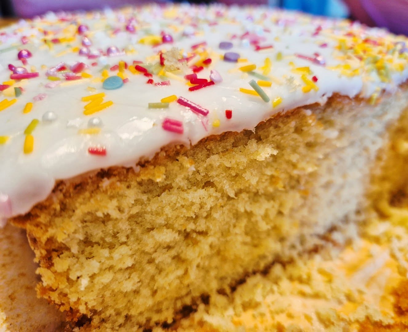 Extreme close-up of a sliced vanilla sponge cake with white icing and rainbow sprinkles